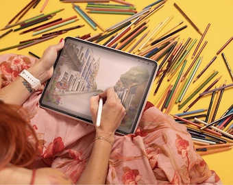 Può includere: Un tablet che mostra un'illustrazione digitale di una scena di strada con edifici e alberi, disegnata con uno stilo bianco. Il dispositivo è circondato da numerosi matite colorate sparse su una superficie gialla a tinta unita.