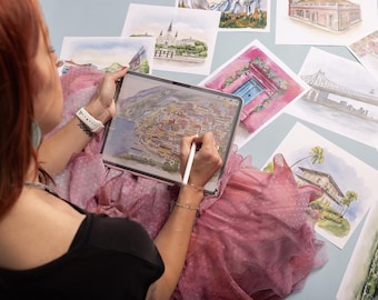 Può includere: Un tablet digitale che mostra un'illustrazione dettagliata in stile acquerello di una città costiera, tenuto da una persona che utilizza uno stilo bianco. Diverse altre stampe ad acquerello di vari paesaggi ed edifici sono sparse attorno al tablet.