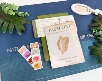 Puede incluir: Un pasaporte con un diseño de arpa y el texto "To a wedding celebration in Ireland" descansa sobre un libro azul. También hay una tarjeta de embarque y sellos con imágenes de flores. Una etiqueta de equipaje blanca y vegetación completan la escena.