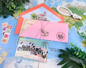 Può includere: Una busta rosa legata con spago rosa e bianco con un ciondolo a forma di ancora in legno, una busta arancione con illustrazione di una casa, una cartolina di Key West Florida, francobolli floreali e un'etichetta per bagagli su una mappa.