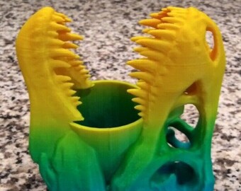 May include: A 3D printed dinosaur head pencil holder with a gradient of blue, green, and yellow.