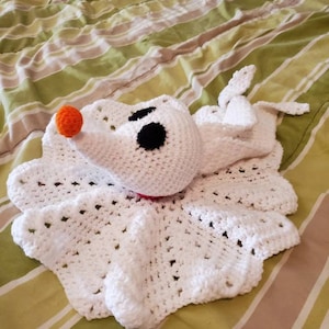 May include: White crocheted blanket with a crocheted ghost character in the center. The ghost has black eyes and an orange nose.