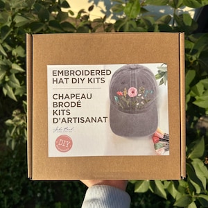 May include: A brown cardboard box featuring a label for embroidered hat DIY kits. The label displays a grey baseball cap with floral embroidery and includes the text Embroidered Hat DIY Kits, Chapeau Brodé Kits D'Artisanat, and DIY.