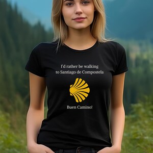May include: Black t-shirt with white text that reads "I'd rather be walking to Santiago de Compostela" and a yellow scallop shell symbol. The text "Buen Camino!" is below the shell.