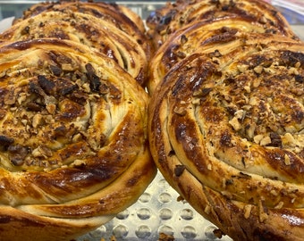 May include: Close-up of several golden brown pastries topped with chopped nuts. The pastries are arranged in a row on a silver tray.