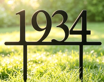 May include: A black metal garden stake featuring the numbers 1934 in a bold, sans-serif font. The numbers are connected by a horizontal bar and supported by two vertical prongs designed for insertion into the ground for outdoor display.