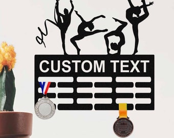 May include: Black metal medal display with silhouettes of four gymnasts. The display has 12 hooks for medals and a space for a personalized inscription. The text "CUSTOM TEXT" is printed on the display.