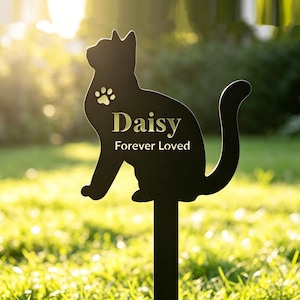 May include: Black metal cat-shaped garden stake with the name "Daisy" and the words "Forever Loved" in gold lettering. A paw print is above the name. The stake is in a grassy area.