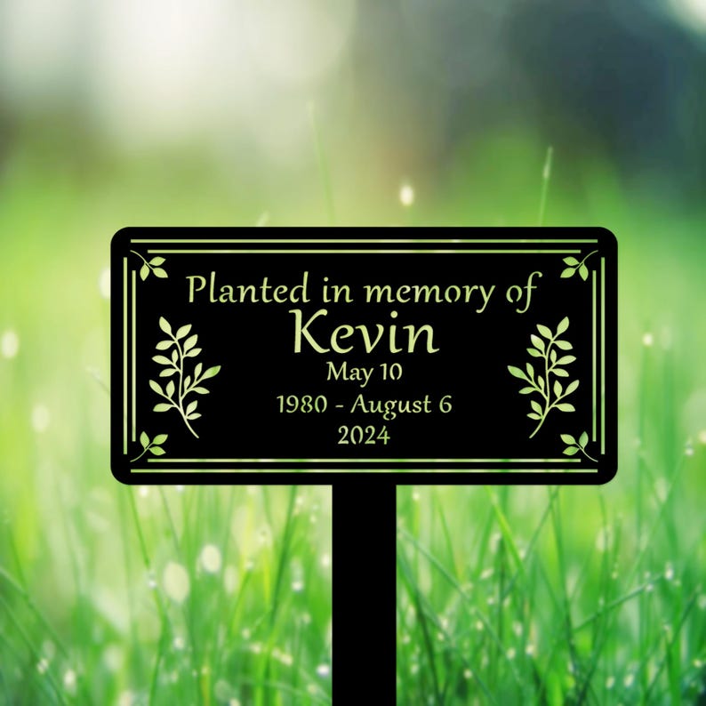 May include: Black metal garden marker with the text "Planted in memory of Kevin May 10 1980 - August 6 2024" and a leafy design.
