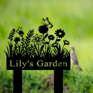 Puede incluir: Se&ntilde;al de jard&iacute;n de metal negro con una silueta de flores, mariposas y hierba. La se&ntilde;al dice "Lily's Garden".