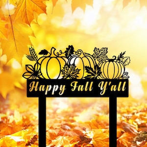 Könnte beinhalten: Schwarzes Metallschild mit dem Text "Happy Fall Y'all" in goldener Schrift. Das Schild zeigt ein dekoratives Design aus Kürbissen und Herbstblättern. Der Hintergrund ist ein verschwommenes Bild von Herbstblättern.