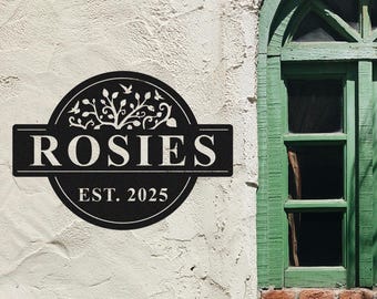 Peut inclure: Une enseigne en métal noir avec le nom "ROSIES" et l'année "EST. 2025" en blanc. Le design circulaire comprend un motif décoratif de fleurs et d'oiseaux. L'enseigne est fixée sur un mur blanc texturé.
