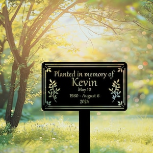 May include: Black metal garden sign with gold lettering that reads "Planted in memory of Kevin May 10 1980 - August 6 2024". The sign has a leafy design and is mounted on a black metal stake.