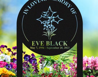 May include: Black metal memorial garden stake with the text "IN LOVING MEMORY OF" and "EVE BLACK" with birth and death dates. The stake features a cross design with floral accents and is set in a colorful flower garden.