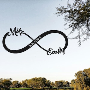 Peut inclure: Symbole infini en métal noir avec les noms "Mike" et "Emily" en écriture cursive. La date "5/20/2025" est centrée dans la boucle infinie. Le fond est un ciel bleu clair avec des arbres.