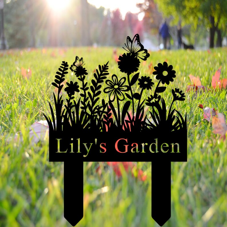 Puede incluir: Letrero de jard&iacute;n de metal negro con una silueta de flores, mariposas y hierba. El letrero dice "Lily's Garden".