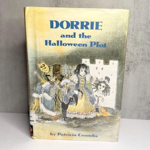 May include: A hardcover book titled Dorrie and the Halloween Plot by Patricia Coombs. The cover features a yellow and white illustration of a character in a dress, a black cat, and masks against a castle background with blue text.