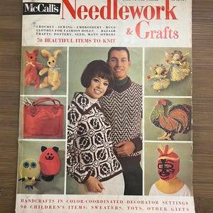 May include: A vintage McCall's Needlework & Crafts magazine cover from Autumn-Winter 1965-66. The cover features a collage of handmade crafts, including knitted sweaters, stuffed animals, and a rooster. The magazine's title is in bold red and white lettering.