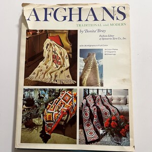 以下が含まれることがあります： 「AFGHANS」というタイトルのヴィンテージ本。副題は「TRADITIONAL and MODERN」、著者はBonita Bray。表紙には、花柄や幾何学模様など、さまざまな色と模様のアフガンが写っています。