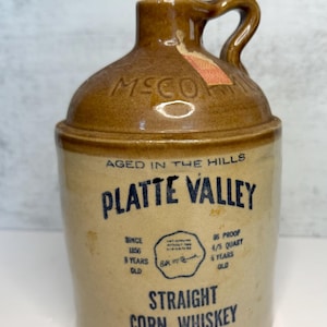 May include: Vintage brown ceramic jug with a handle, featuring the text "PLATTE VALLEY STRAIGHT CORN WHISKEY". The jug has a capacity of 4/5 quart and is aged 5 years. The design includes a label and the text "AGED IN THE HILLS".
