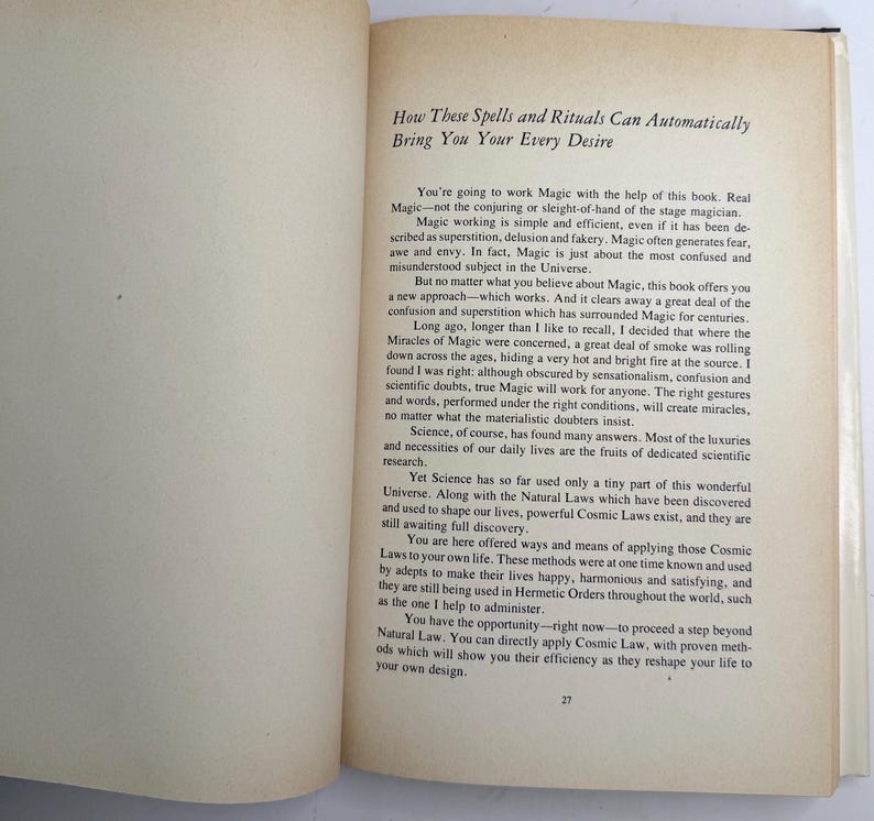 May include: Open book with text titled "How These Spells and Rituals Can Automatically Bring You Your Every Desire." The page has paragraphs of text with the number 27 at the bottom. The book is open on a white surface.