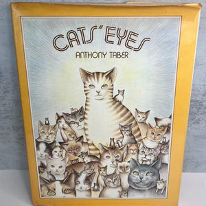 May include: A vintage book titled "Cats' Eyes" by Anthony Taber. The cover features a large tabby cat surrounded by numerous smaller cats of various breeds and colors. The background is a light blue with a yellow border.