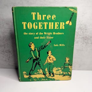 May include: Vintage hardback book titled "Three Together" with a green cover and yellow lettering. The cover features an illustration of three children and a drawing of an aeroplane. The book tells the story of the Wright Brothers and their sister.