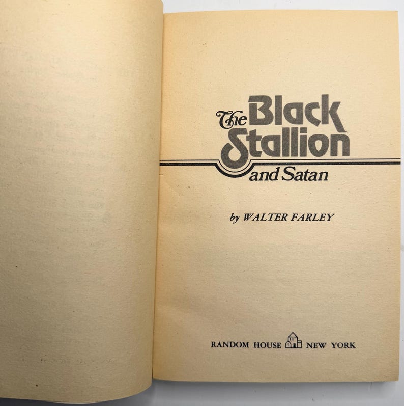 May include: Open book with the title "The Black Stallion and Satan" by Walter Farley. The title is in a stylized black font with a decorative swirl. The book is published by Random House, New York.