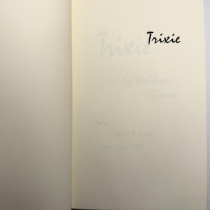 May include: Open book pages with the title "Trixie" in black ink. The author's name and publisher's information are also visible in light grey ink. The book's pages are a cream colour.