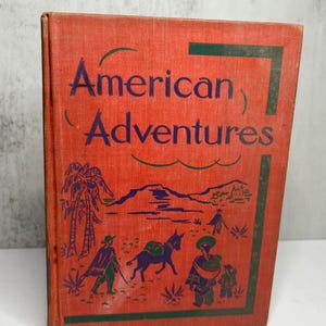 May include: A vintage book titled "American Adventures" with a red cover and green border. The cover features illustrations of people, a donkey, and palm trees. The title is in dark blue lettering.