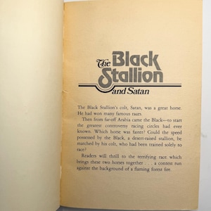 May include: Open book page featuring the title "The Black Stallion and Satan" in a stylized black and white font. The text describes a horse race between two horses, the Black and Satan, with a fiery background.