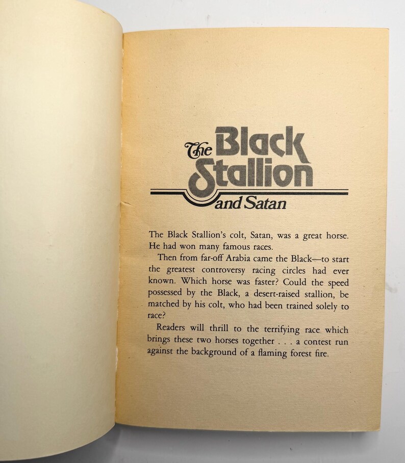 May include: Open book page featuring the title "The Black Stallion and Satan" in a stylized black and white font. The text describes a horse race between two horses, the Black and Satan, with a fiery background.
