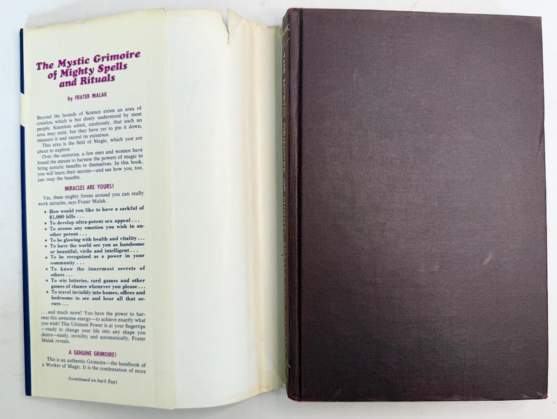 May include: An open book titled "The Mystic Grimoire of Mighty Spells and Rituals" by Frater Malak. The book has a dark brown cover and white pages with text. The left page has text in purple and blue.