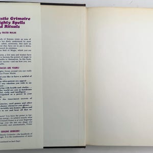 May include: Open book titled "The Mystic Grimoire of Mighty Spells and Rituals" by Frater Malak. The cover is dark blue with white text. The open pages are off-white with black text describing the book's contents.