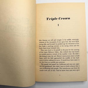 May include: Open book pages with the title "Triple Crown" and the number "1" at the top. The text describes a horse race, mentioning Alec Ramsay, racing silks, and the Belmont Stakes. The page has a cream color.