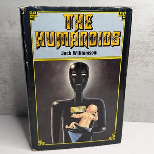 May include: A vintage paperback book titled "The Humanoids" by Jack Williamson. The cover features a black humanoid figure holding a baby, with the title in yellow and black against a light blue background.