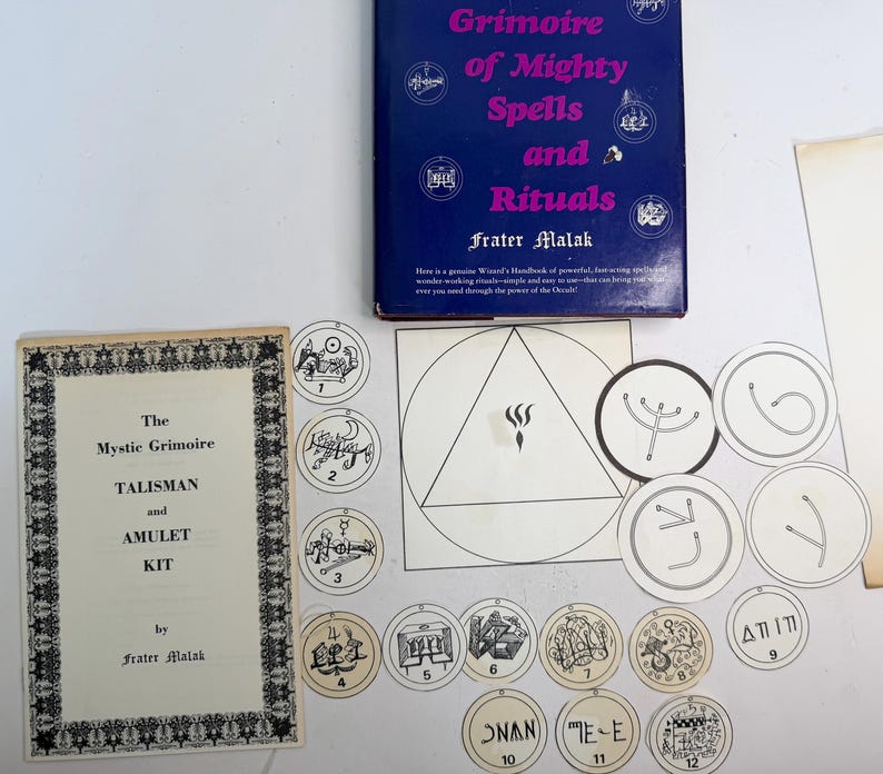 May include: A collection of mystical items including a book titled "Grimoire of Mighty Spells and Rituals" and a booklet labeled "The Mystic Grimoire Talisman and Amulet Kit." Also included are several circular tokens and a geometric diagram.