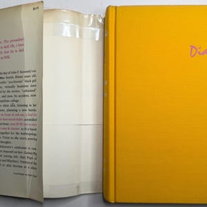 May include: A yellow hardcover book titled "Diary" in pink script. The book is open, showing white pages and text on the inside cover. The spine of the book is also yellow. The book's cover is plain.