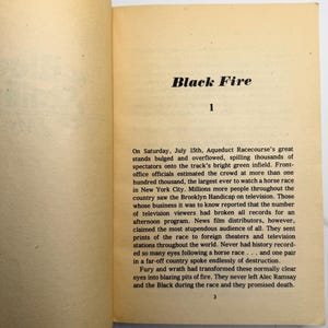 May include: Open book pages with the title "Black Fire" at the top. The text describes a horse race at Aqueduct Racecourse, with details about the crowd and television viewership. The page number "1" is visible.