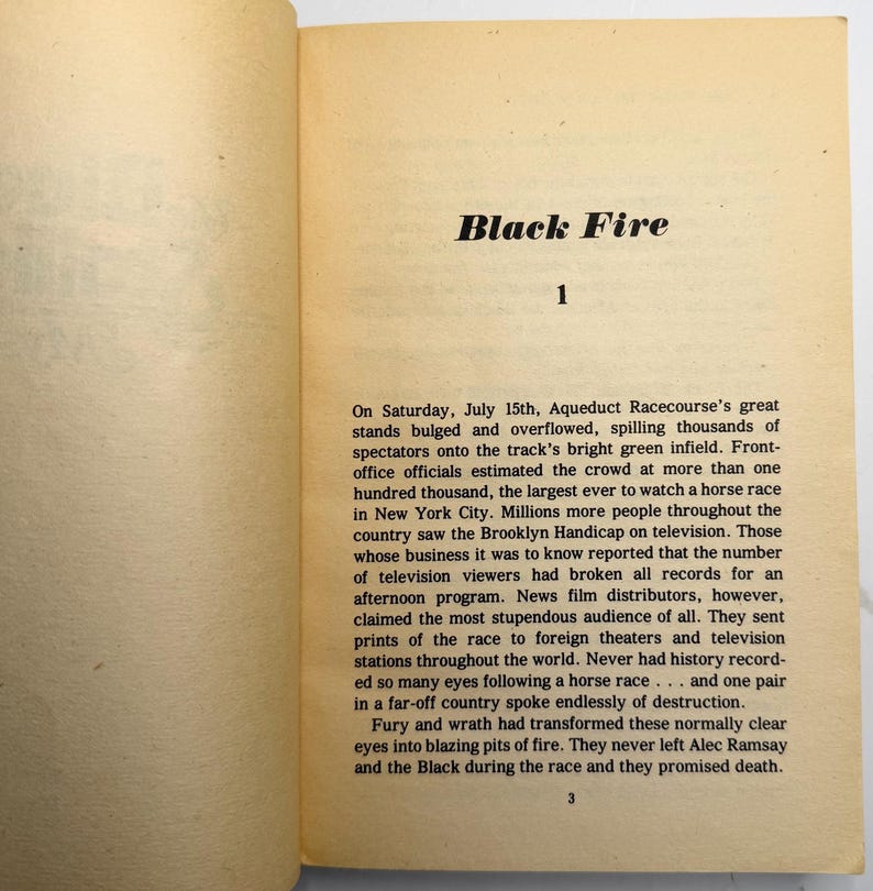 May include: Open book pages with the title "Black Fire" at the top. The text describes a horse race at Aqueduct Racecourse, with details about the crowd and television viewership. The page number "1" is visible.