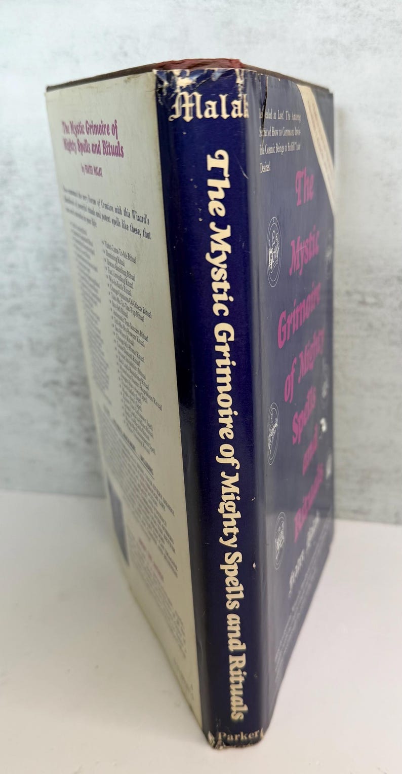 May include: A vintage book titled "The Mystic Grimoire of Mighty Spells and Rituals" by Peter Malak. The book has a blue spine with white text and a cream-colored cover. The book's title is also printed on the cover in pink.