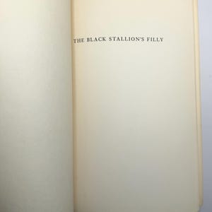 May include: Open book with the title "THE BLACK STALLION'S FILLY" printed in black on a cream-colored page. The book is open to a double-page spread, with the text centered on the right-hand page.