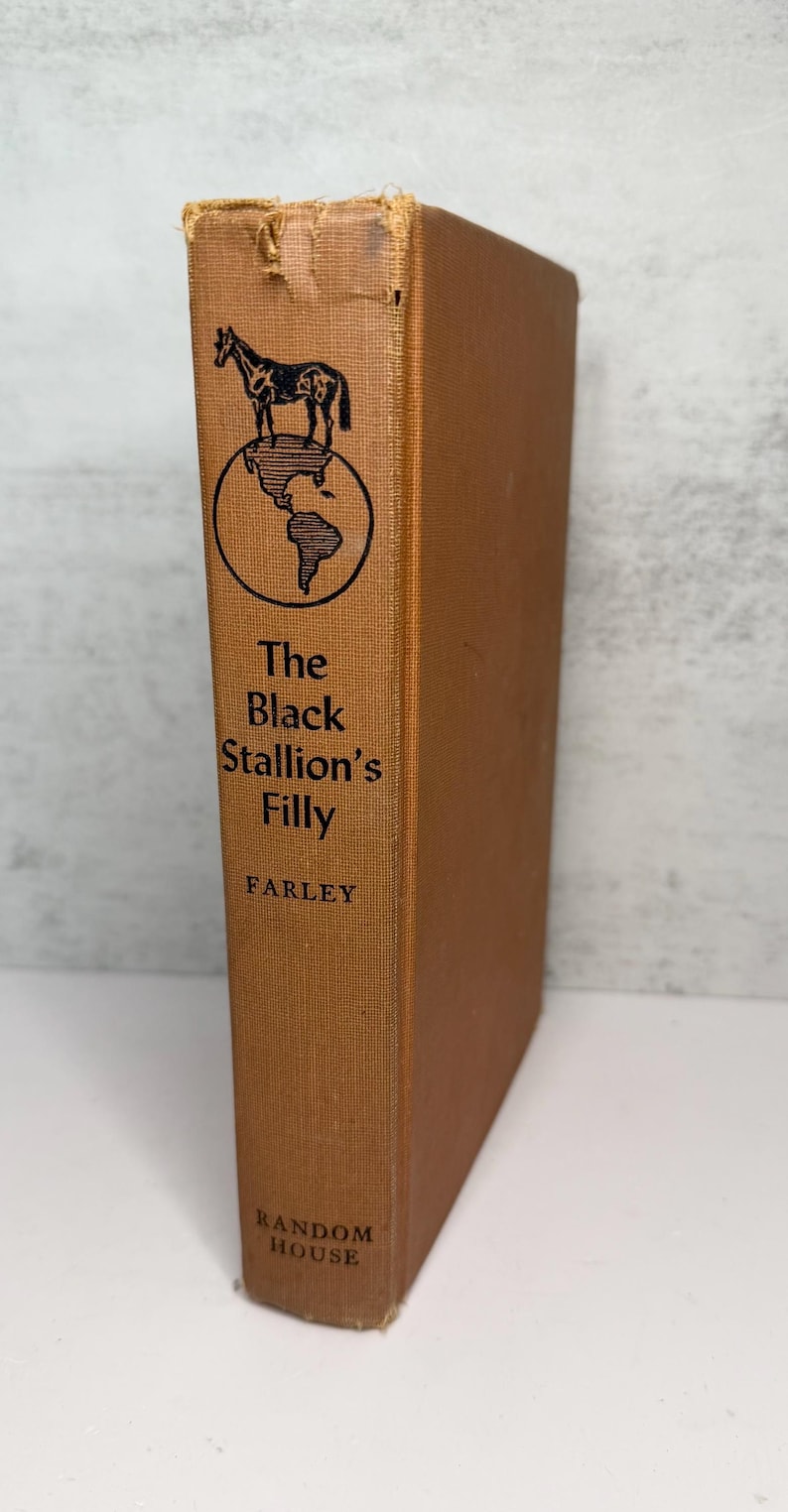 May include: A vintage hardcover book titled "The Black Stallion's Filly" by Farley. The book has a brown cover with a black illustration of a horse above a globe. The publisher's name, Random House, is at the bottom.
