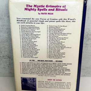 May include: The Mystic Grimoire of Mighty Spells and Rituals by Frater Malak. The book cover lists various spells and rituals, including those for wealth, love, and success. The cover is white with black and purple text.