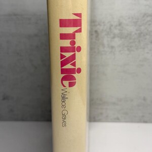 May include: A hardback book titled "Trixie" by Wallace Graves. The title is in large, pink letters. The book has a beige cover and is wrapped in clear plastic. The publisher's logo is visible at the bottom.