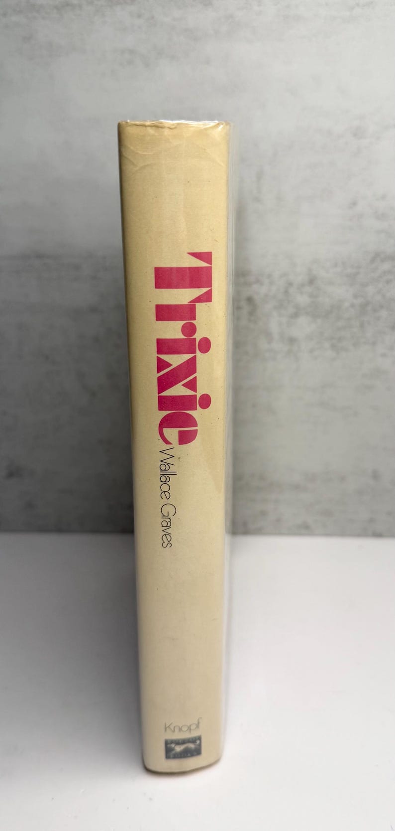 May include: A hardback book titled "Trixie" by Wallace Graves. The title is in large, pink letters. The book has a beige cover and is wrapped in clear plastic. The publisher's logo is visible at the bottom.