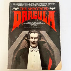 May include: The Annotated Dracula book cover featuring a portrait of Dracula in a black coat and white bow tie. The title is in large red letters, with text that reads "Forged from Folklore and Authentic History - The Greatest Horror Story Ever Told."