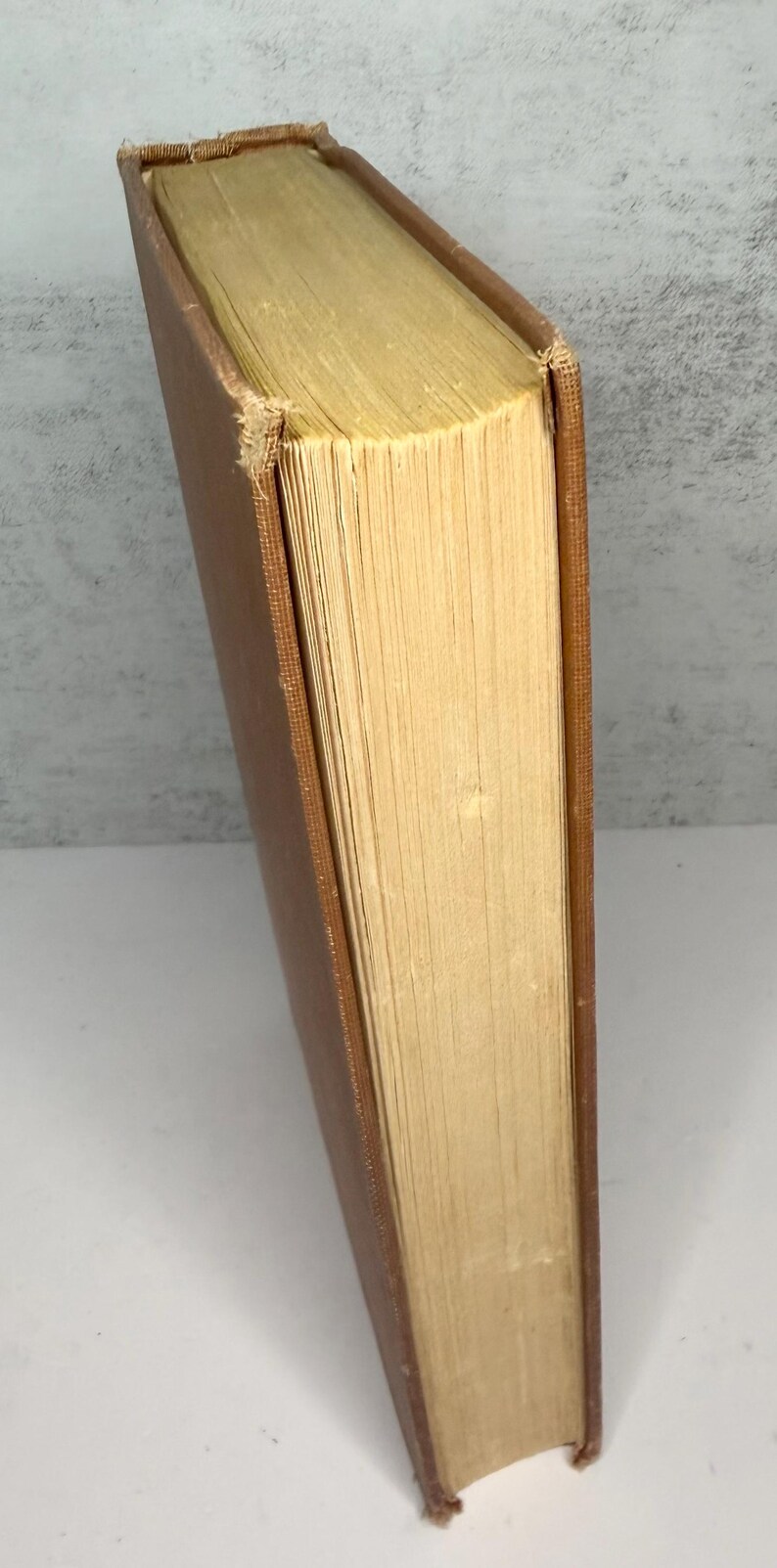 May include: A vintage book with a brown cover and aged, yellowed pages. The book's spine is visible, showing the binding and the wear and tear of time. The pages are thick and have a rough texture, suggesting age and use.