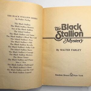 May include: Open book with the title "The Black Stallion Mystery" by Walter Farley. The book's cover features a stylized logo with the words "Black Stallion" in a decorative font. The left page lists other books in the series.