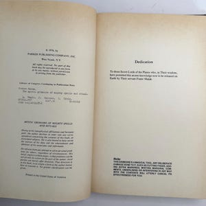 May include: Open book with text on aged paper. The left page includes publishing information, Library of Congress data, and the title "MYSTIC GRIMOIRE OF MIGHTY SPELLS AND RITUALS." The right page has a dedication. A note at the bottom warns against damaging the book.